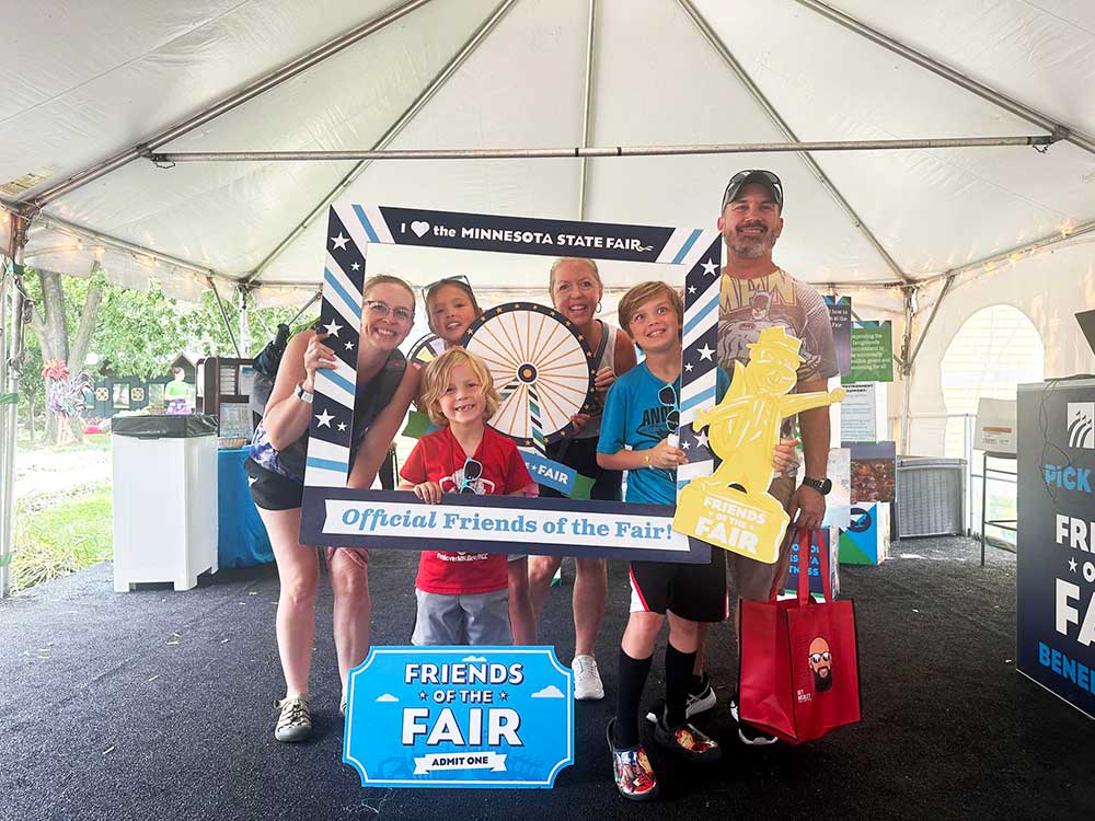 A family stands behind a Friends of the Fair photo frame to pose for a photo.