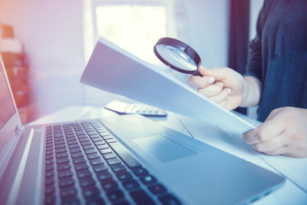 Woman holding magnifying glass over paperwork