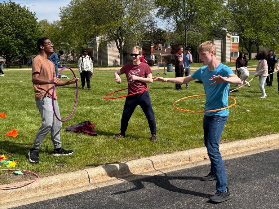 3 students hula hoop on a grassy field