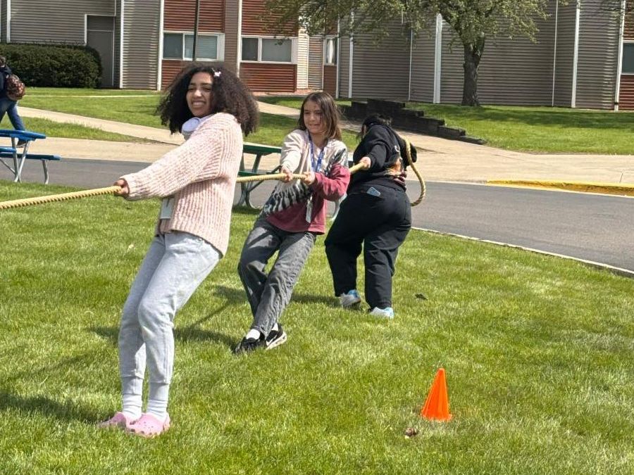 3 students pull on a rope during tug of war in ag rassy field