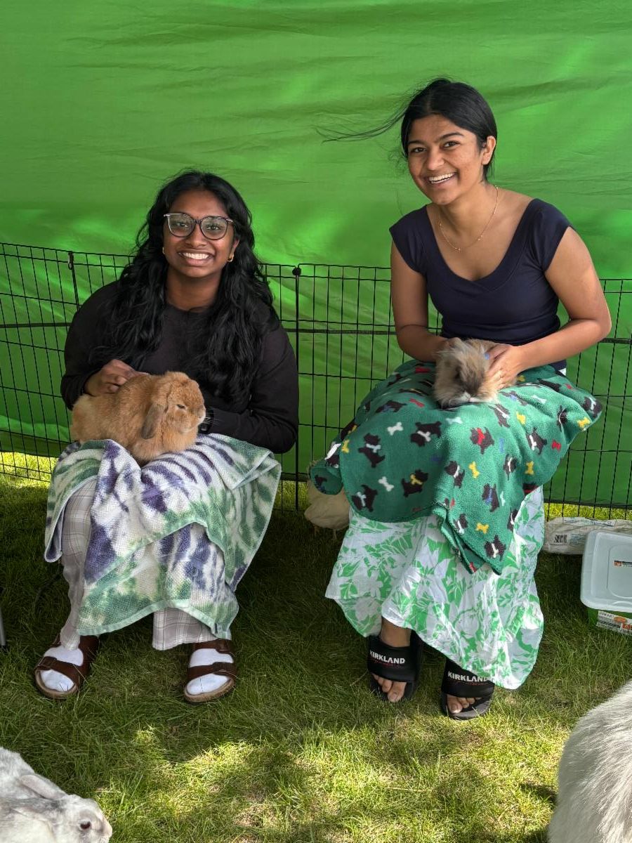Two students hold live rabbits while smiling at a petting zoo