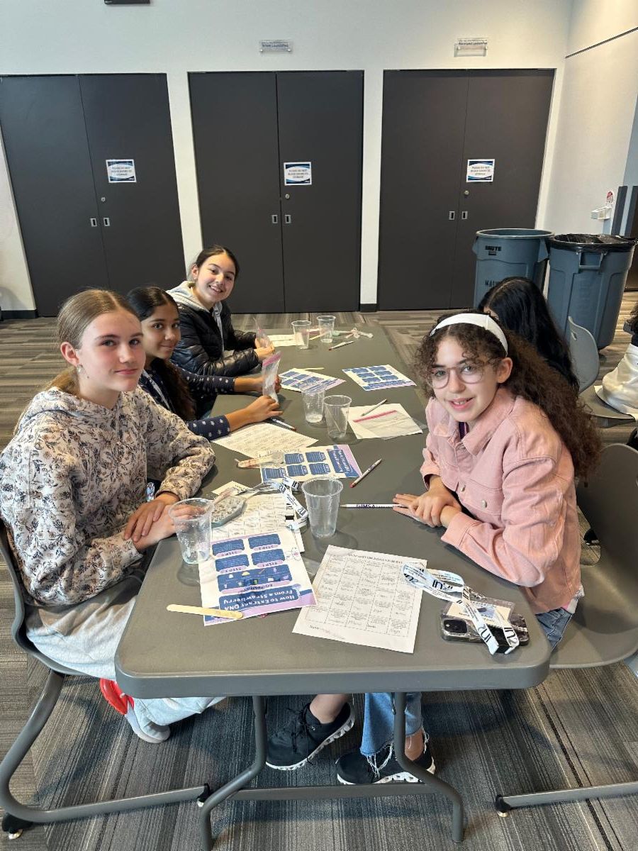 three girls sit at a table surrounded by papers and supplies for science experiments