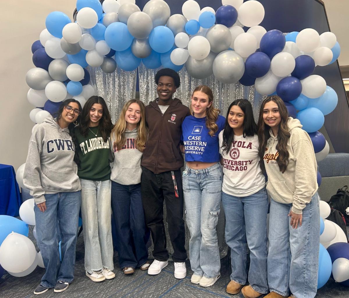 Students pose in college sweatshirts in front of blue and white balloons