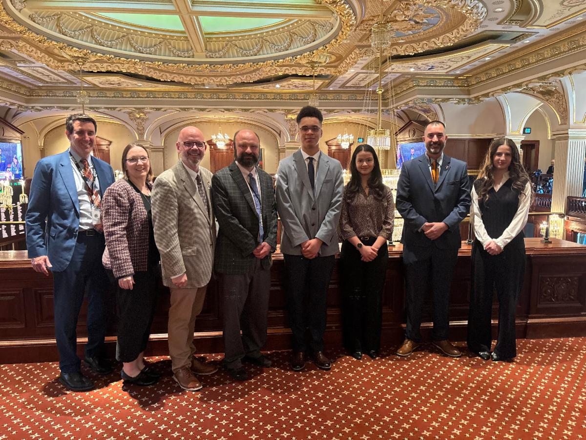 Students in business professional attire post in the Illinois State Senate Chamers with members of the Senate
