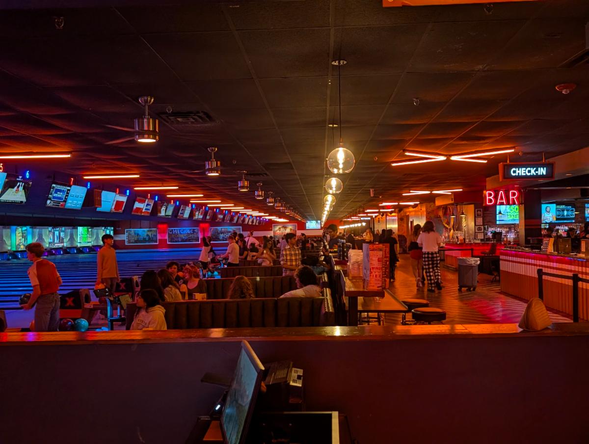 Wide shot of a dark lit bowling alley where students are bowling