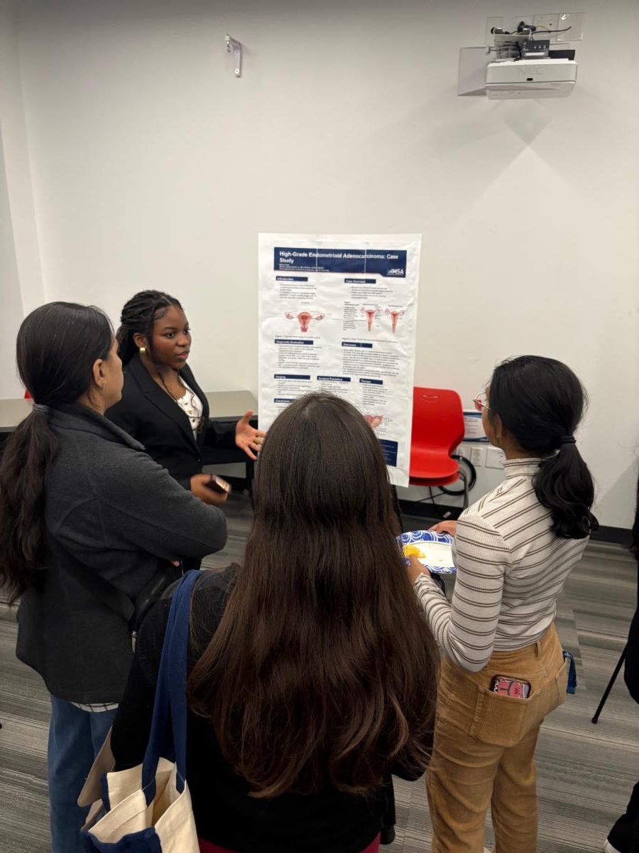 A student in business formal attire stands in front of a poster presenting to three other students. 