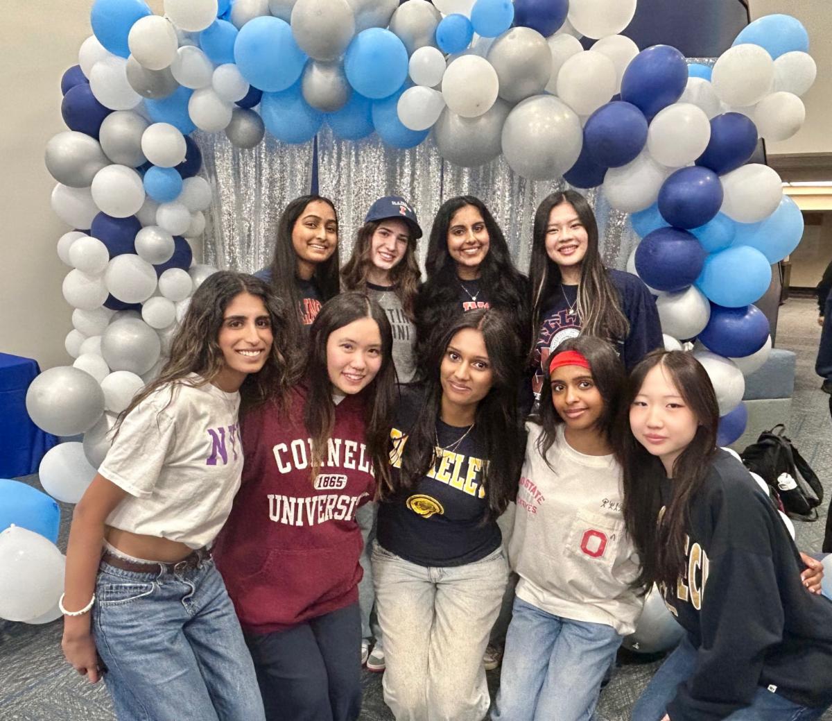Students pose in college sweatshirts in front of blue and white balloons