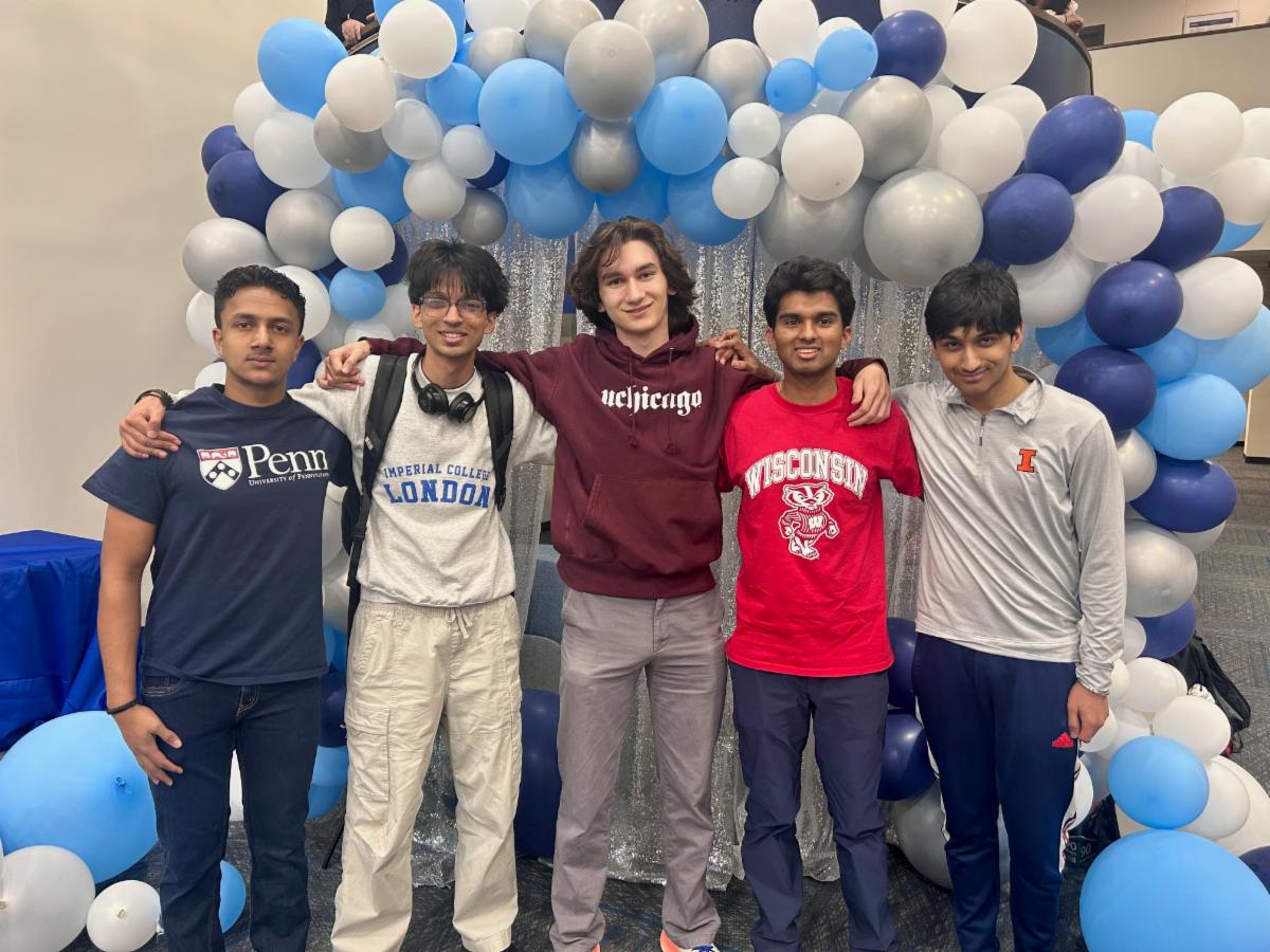 Students pose in college sweatshirts in front of blue and white balloons