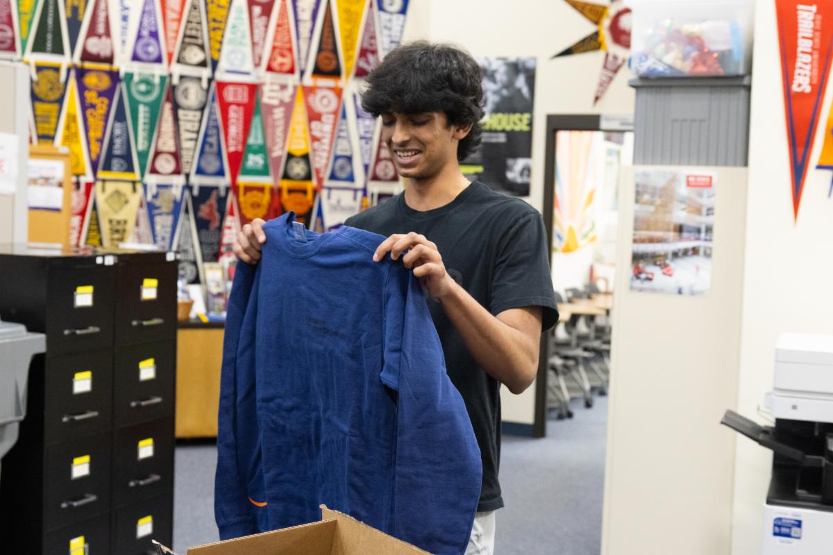 A student holds smiels as he holds up a sweatshirt standing in a room with college penants decorating the walls. 