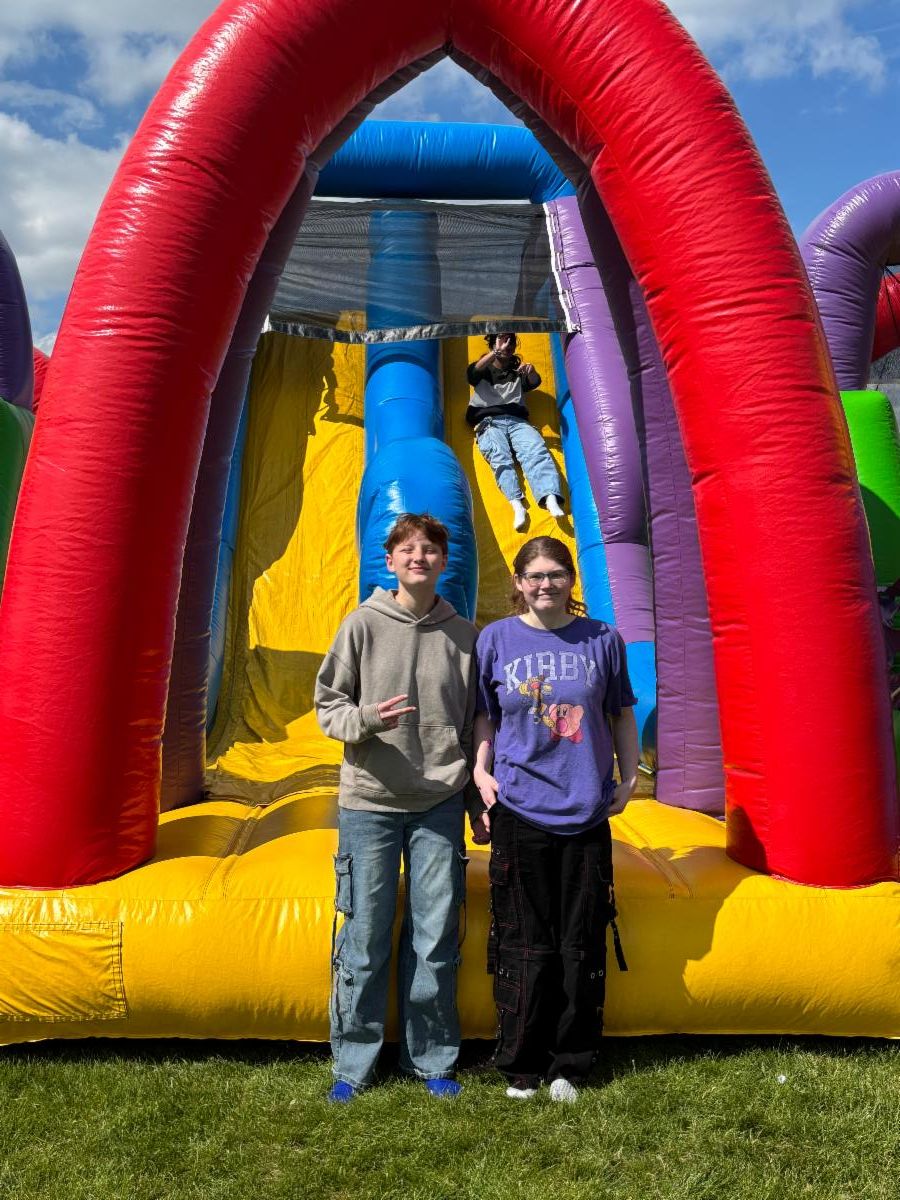 Students pose in front of an inflatable slide while another student goes down teh slide behind them