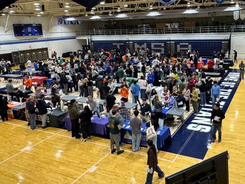 Aerial shot of a gynmasium filled with info boohts and people visiting for a college fair. 