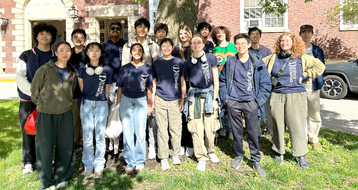 The Science Olympiad team poses for a picture outside of a brick academic building under a tree