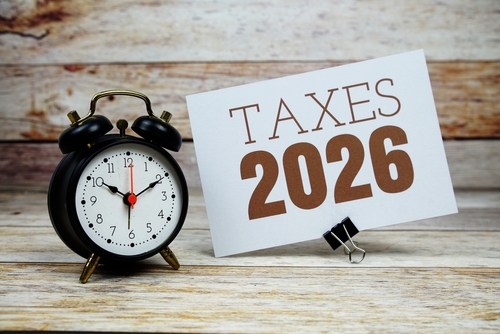Taxes 2026 text with alarm clock on wooden background