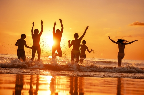 Group of happy young friends are having fun and runs to sunset sea beach over the waves