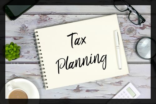 Top view of mobile phone_plant_coffee_calculator_magnifying glass_sunglasses_pen and notebook written with Tax Planning on wooden background.