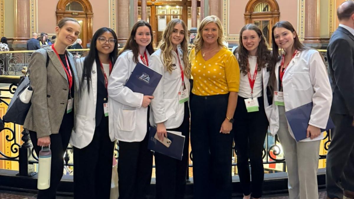 College of Pharmacy students in white coats pose with legislator in the Iowa State capitol building during IPA Pharmacy Day on the Hill.
