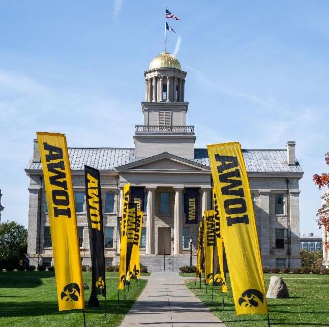 Gold domed Old Capitol building on Iowa City campus with yellow and black flags in the forefront.