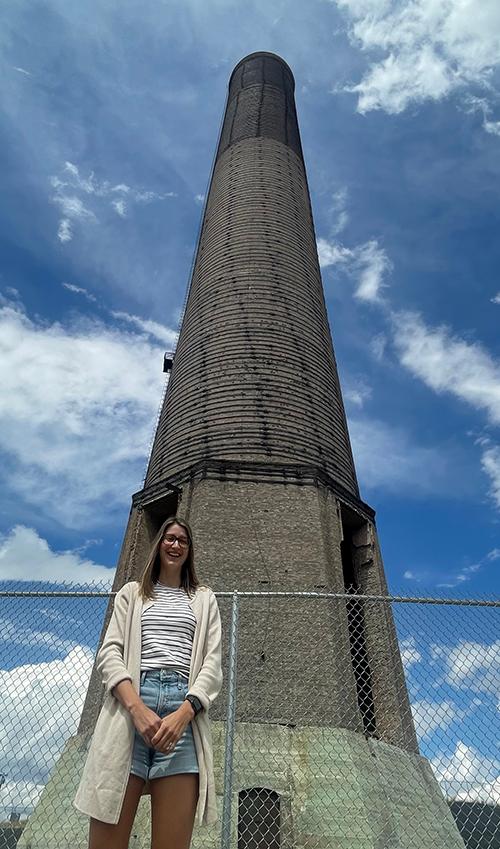 CREWS graduate student Megan Moore stands in front of the Anaconda smelter stack
