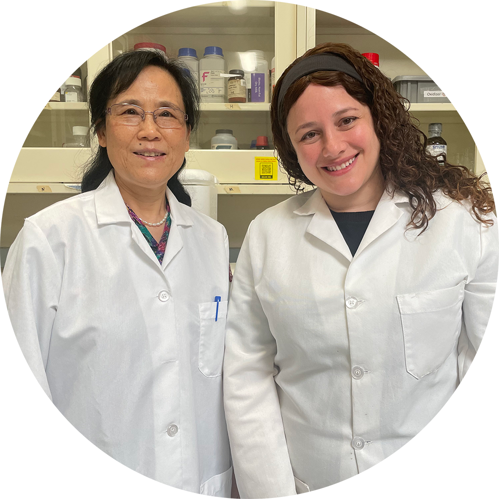 Two women in white lab coats in a lab smiling side by side