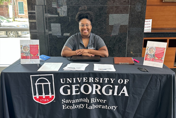 Photo of Tyjaha Steele sitting behind an exhibit booth at a recruitment event