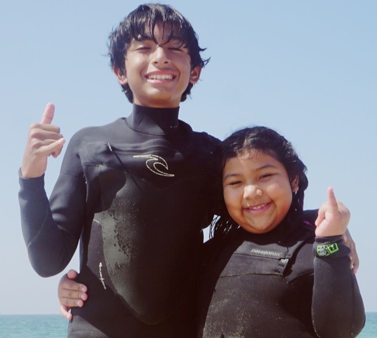 Two children in wetsuits smile for the camera