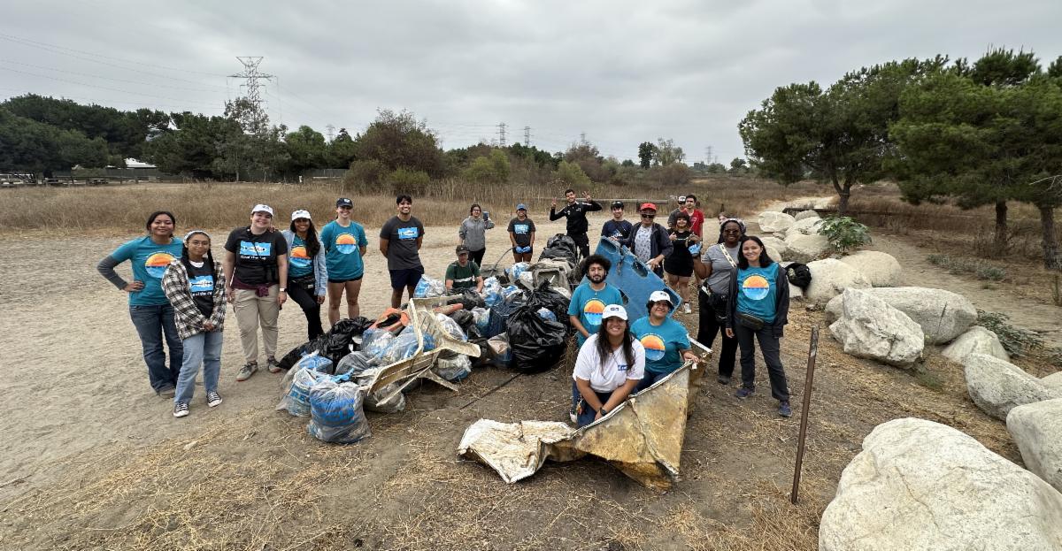 A group of people gather around a large pile of trash they just collected