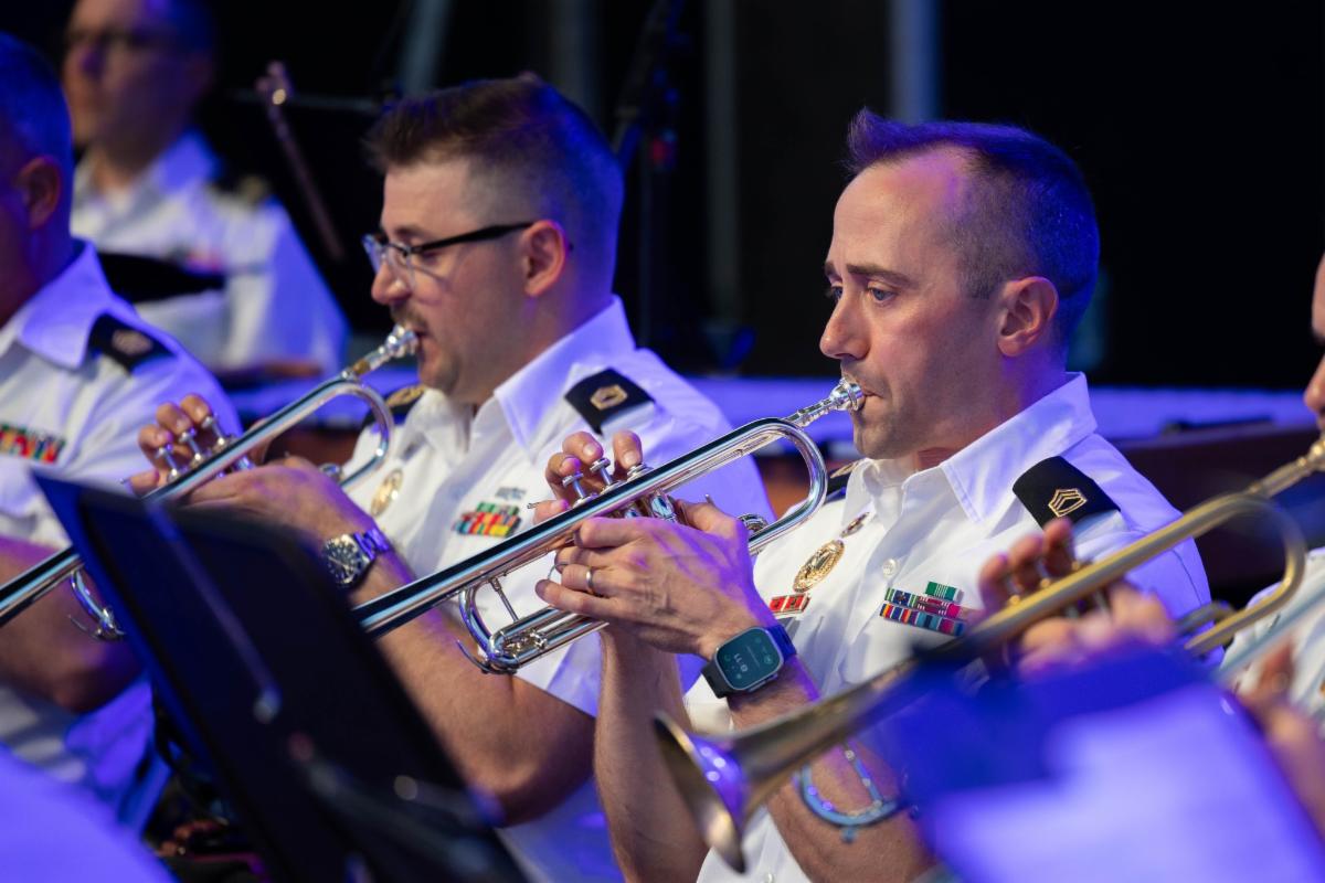 A line of trumpet players at a concert in military stage uniform.
