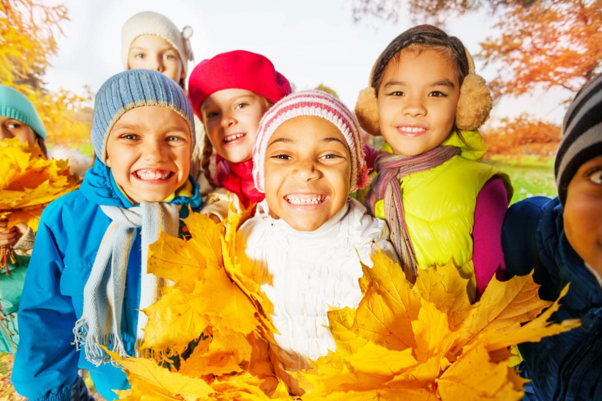 a group of kids smiling and holding autumn leaves