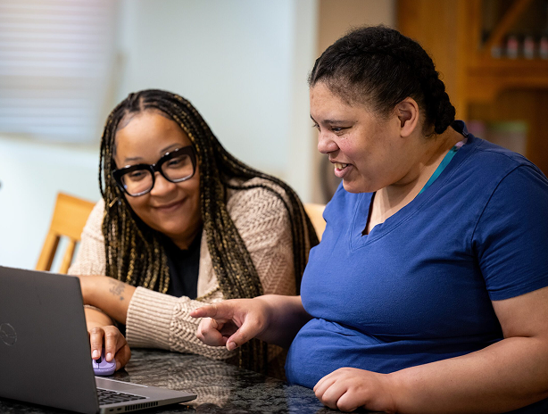 Two people sitting at a table looking at a laptop computer