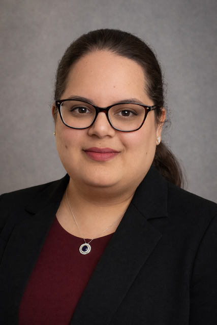 Headshot of Hira. She is wearing black rimmed glasses with a black blazer and maroon shirt