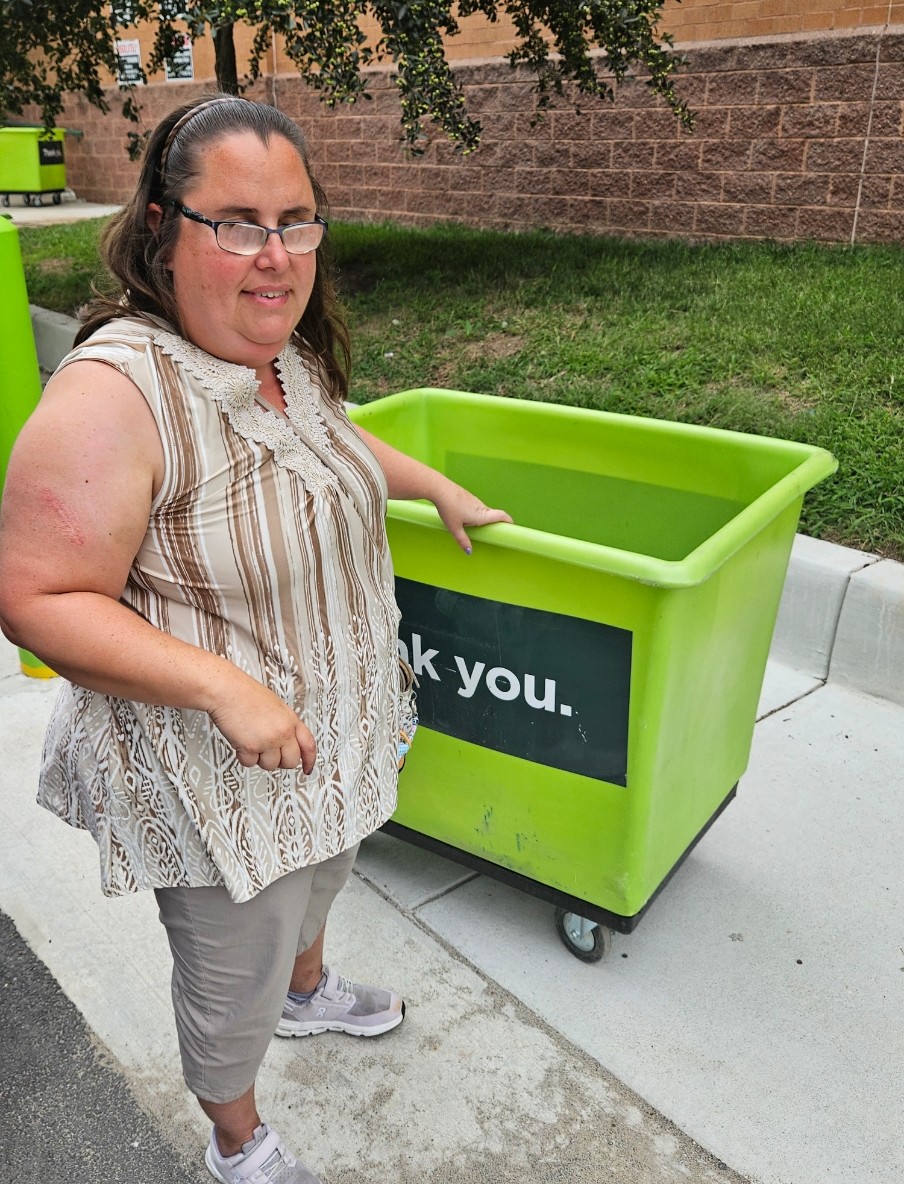 A person stnading next to a big green moving bin
