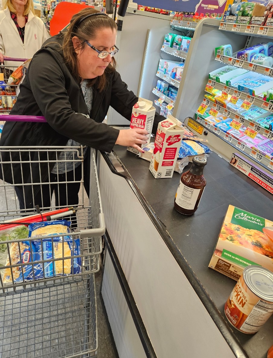 A person wearing a black sweater and glasses loading groceries on a conveyer belt 