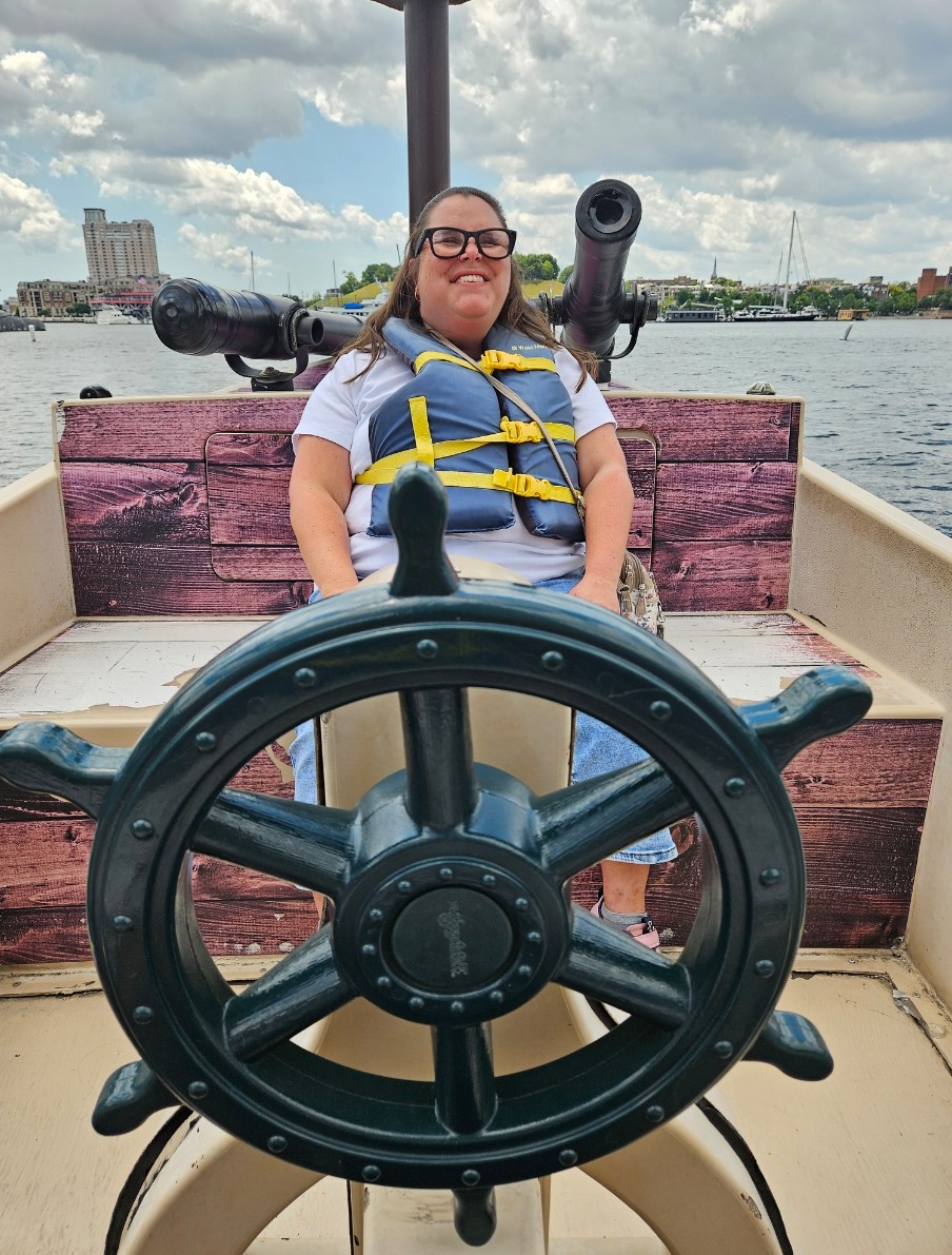 A person wearing a like jacket sitting behind the steering wheel of a ship
