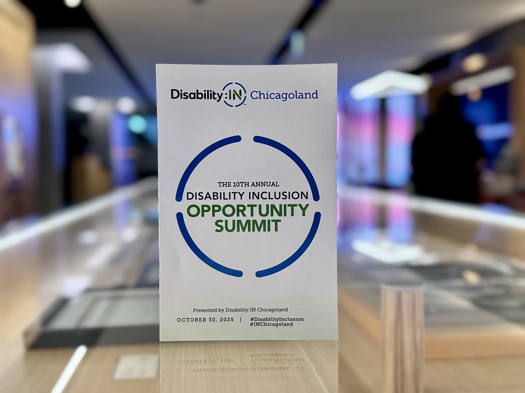 Photo of the event program for the 2025 Disability Inclusion Opportunity Summit standing on a counter with the McDonalds conference space behind it 