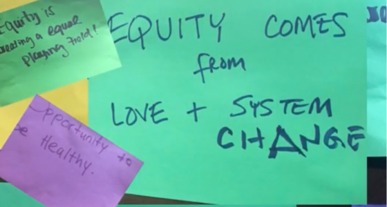 Photo of a green sticky note that reads "Equity comes from love and system change".