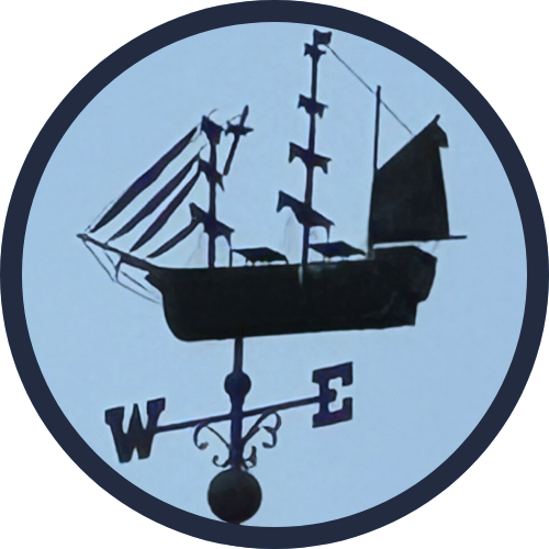 Weather vane in the shape of a sailing ship against a blue background.