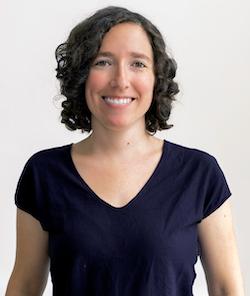 White woman with short, curly, brown hair wearing purple t-shirt