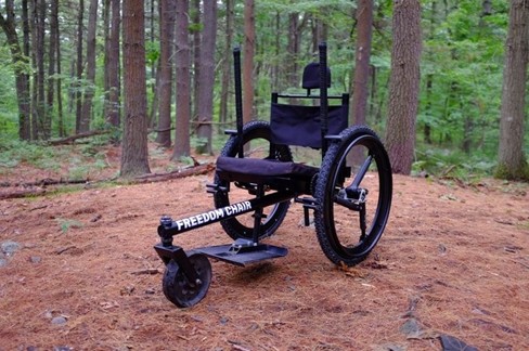 Freedom wheelchair in forest. The wheelchair has oversized, all terrain wheels, push levers, and a small third wheel in front.