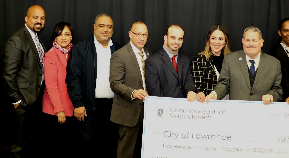 Eight people pose with a giant check against a black backdrop.