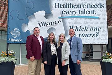 four people standing in front of an Alliance for Healthcare Education sign