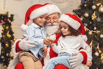 two children smiling while sitting on Santa's lap