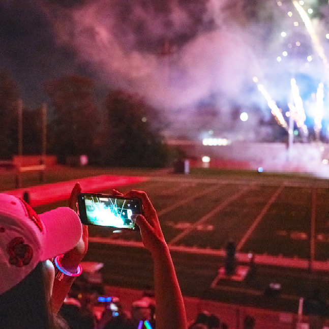 A color photo of a person using their cell phone to take a picture of fireworks