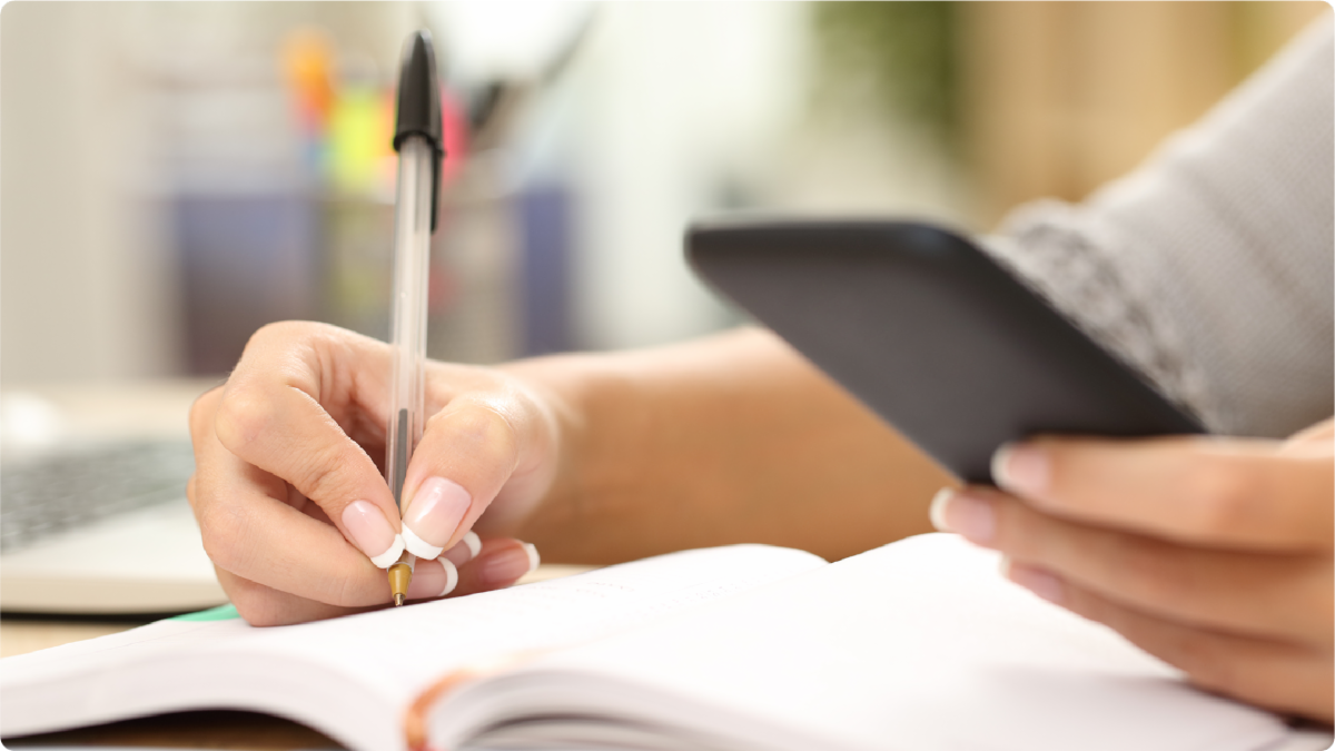A color photo showing a person using a smart phone and writing down notes. Shutterstock