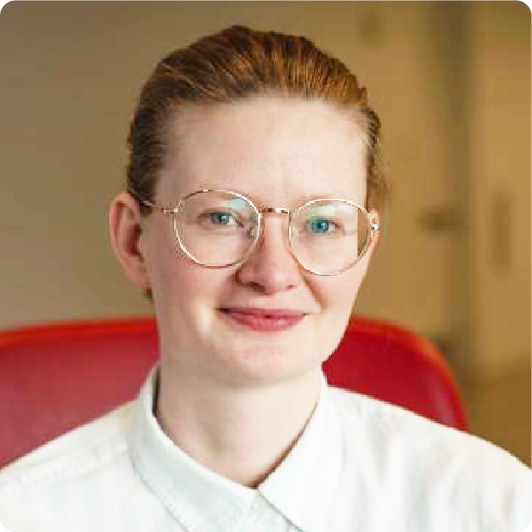 A color photo of a woman with red hair and glasses, smiling for a photo.