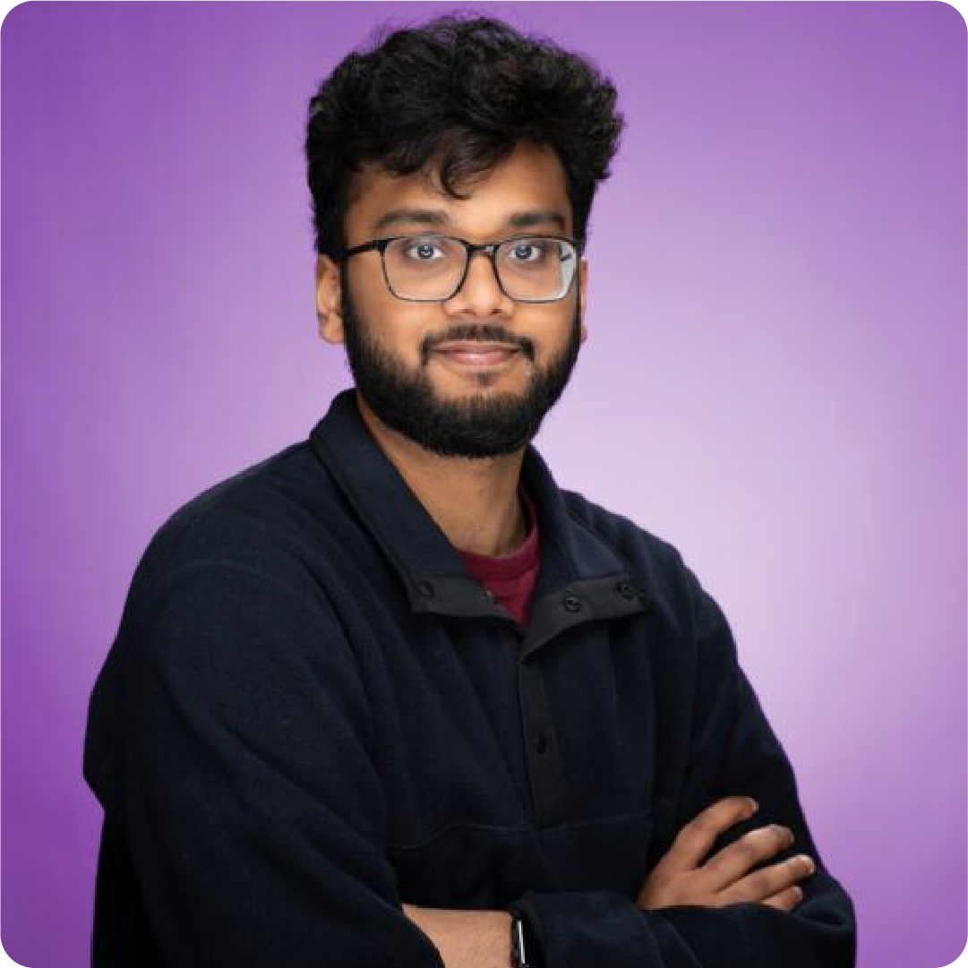 A color photo of a man with a beard and glasses in front of a purple background.