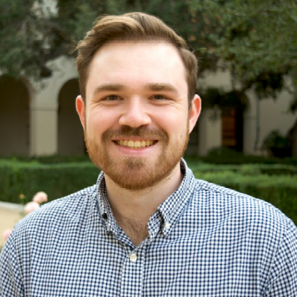 A color photo of a man with a beard smiling for a photo outdoors.