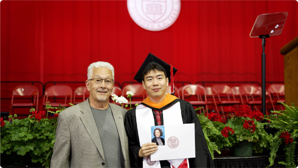A color photo of a recent graduate in regalia with a family member.