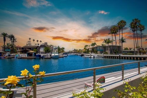 a gorgeous summer landscape at Naples Canals with boats and yachts docked_ luxury homes_ blue ocean water_ lush green palm trees and powerful clouds at sunset in Long Beach California USA