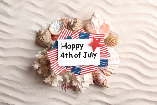 Flat lay composition with greeting card_ USA flags and seashells on sand. Happy Independence Day