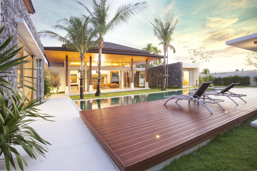 real Exterior design of spacious modern luxury pool villa. Feature wooden decking_ sun bed_ big swimming pool and greenery garden _ home _ house